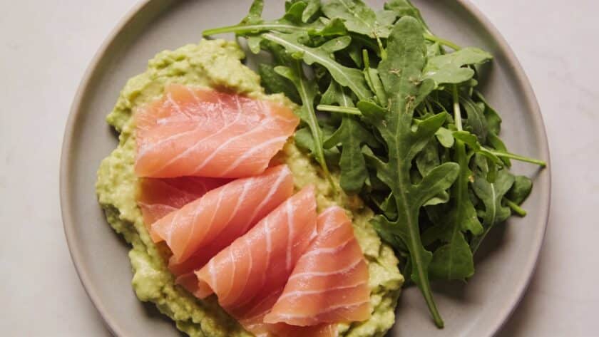 Assiette vue de dessus avec des tranches de saumon fume sur lit de des avocado et feuilles de salade verte