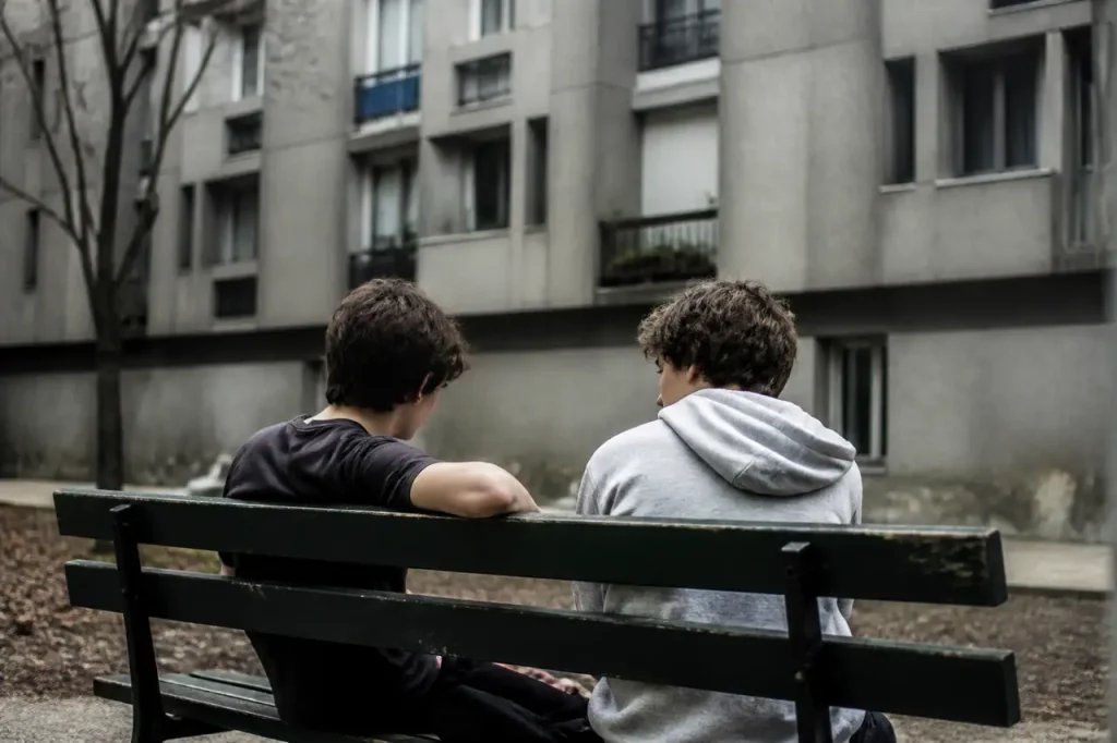 Jeunes assis sur un banc devant immeubles gris